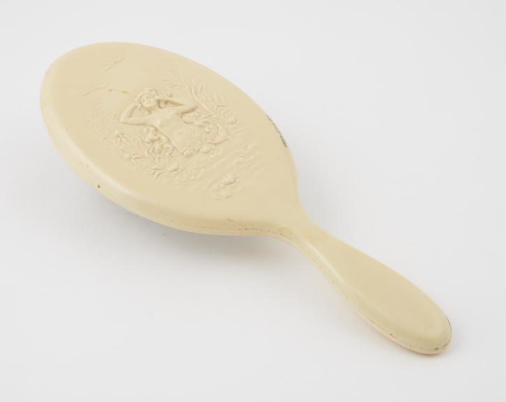 Oval hand mirror of imitation ivory celluloid with an embossed