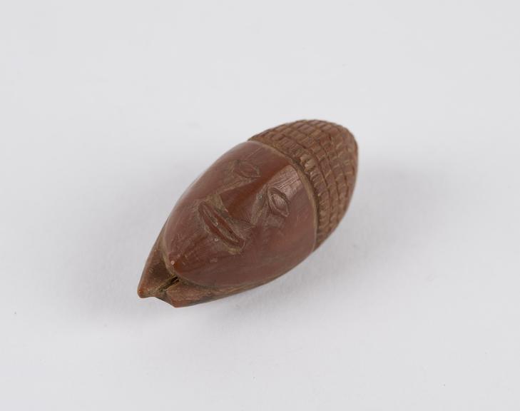 Amulet, in the form of a face, carved from a fruit stone