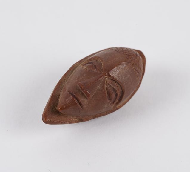 Amulet, in the form of a face, carved from a fruit stone