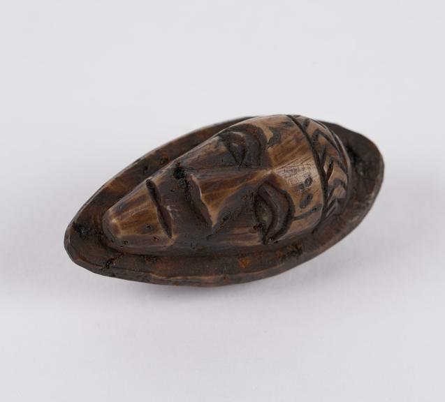 Amulet, in the form of a face, carved from a fruit stone