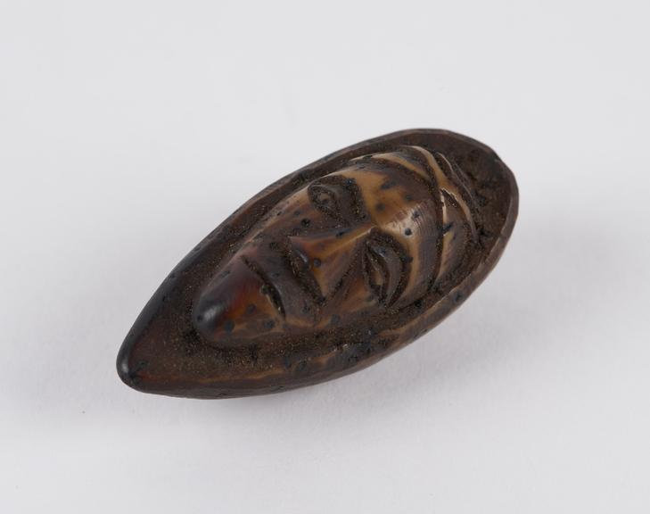 Amulet, in the form of a face, carved from a fruit stone