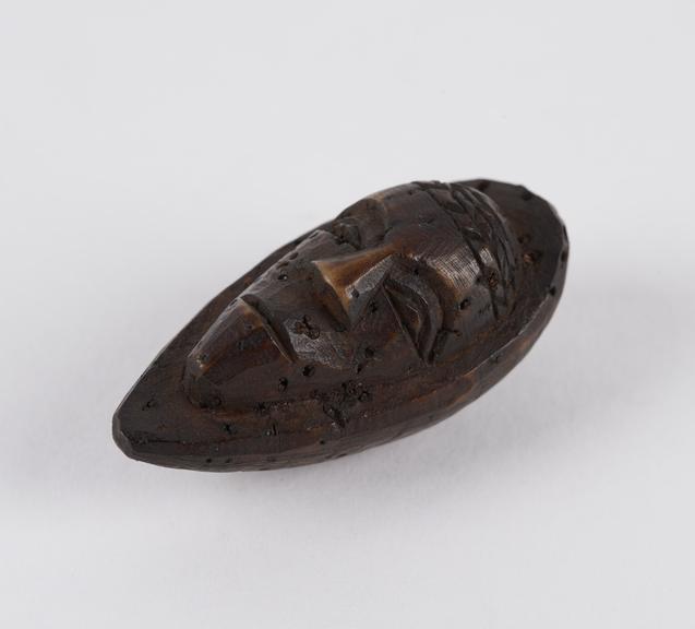 Amulet, in the form of a face, carved from a fruit stone