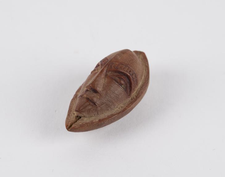 Amulet, in the form of a face, carved from a fruit stone