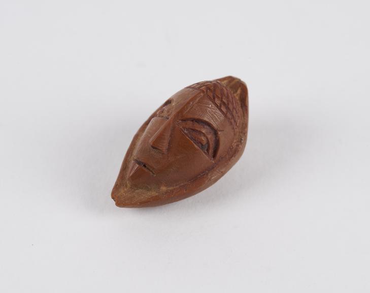 Amulet, in the form of a face, carved from a fruit stone