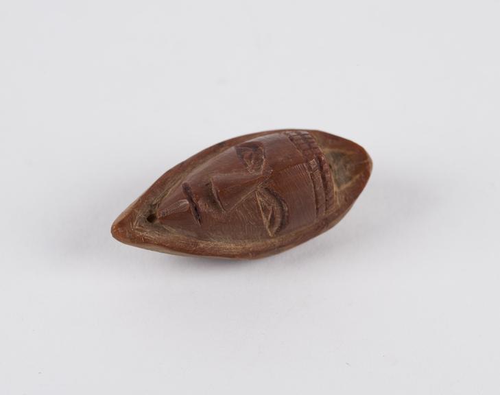 Amulet, in the form of a face, carved from a fruit stone