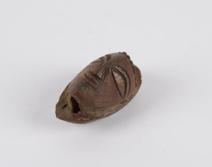 Amulet, in the form of a face, carved from a fruit stone