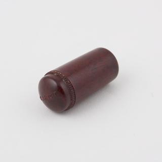 Reddish, small, cylindrical container containing small black object