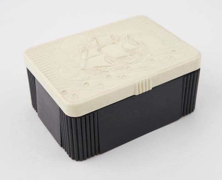 Black rectangulr box with white hinged lid with a sailing ship