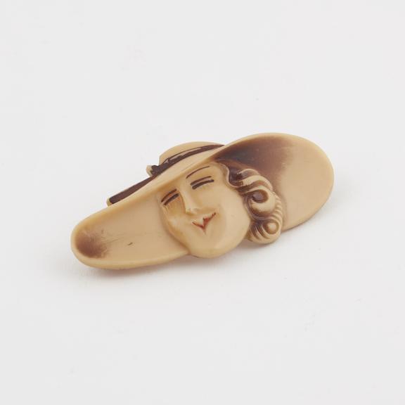 Brooch of moulded buff plastic in form of a woman's head with a