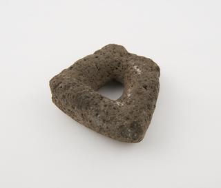 Pestle formed from bruncated triangle of grey porous stone with ovoid finger hole in centre