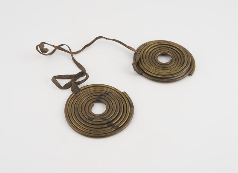 Ornament of two brass coils suspended from leather thong