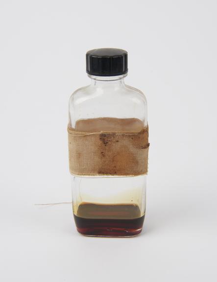 Glass bottle with brown substance and white fabric wrapping.