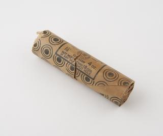 Cylindrical stick of explosive substitute in brown waxed paper wrapper with black printing and black roundel pattern