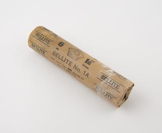 Cylindrical stick of explosive substitute in brown paper wrapper with black printing