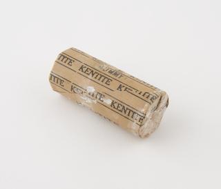 Cylindrical stick of explosive substitute in brown paper wrapper with black printing and trade name patterning