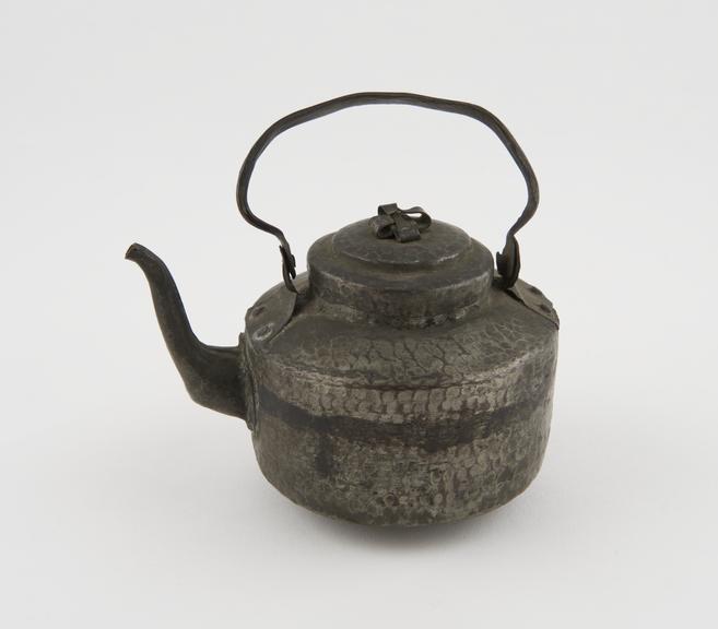 Small teapot of beaten metal with hinged handle