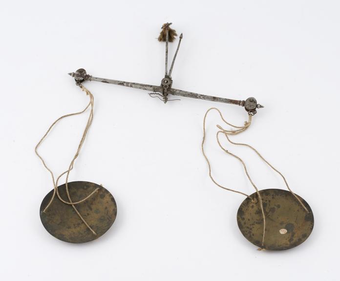 Apothecary's balance with corroded steel beam and brass pans suspended from yellow cords (balances)