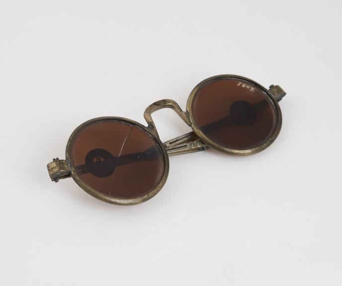 Transverse folding, tinted spectacles, brass, one lens cracked