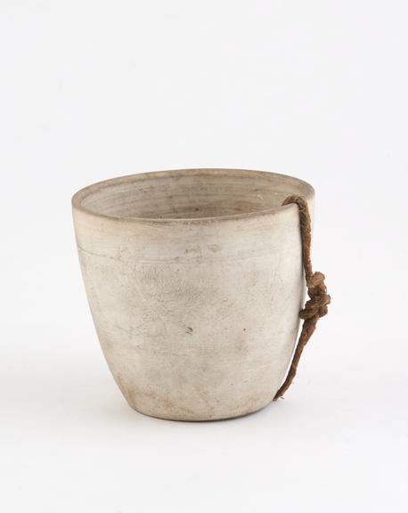 Circular white earthenware crucible, with small hole in base