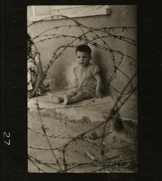 Cypriot child sitting on concrete bench behind barbed wire
