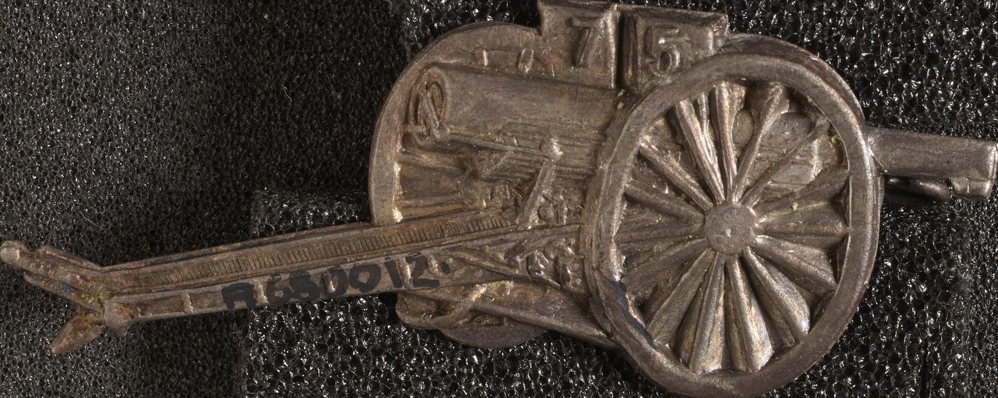 Metal badge in shape of gun and gun carriage