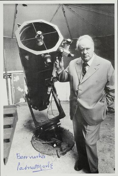 Photograph of Patrick Moore next to his telescope, 1970s