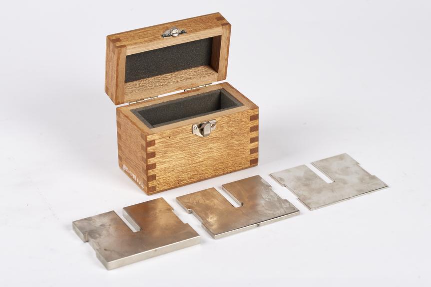 Wooden box with padded inside containing three similar shaped but differing thickness stampings