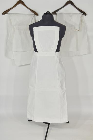 Three white linen aprons with square pin-up bibs and button waists