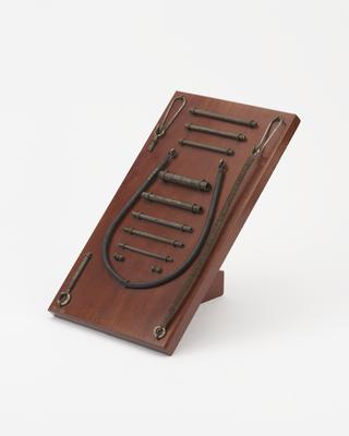 Fourteen specimens of coiled steel bands and cords mounted on a board